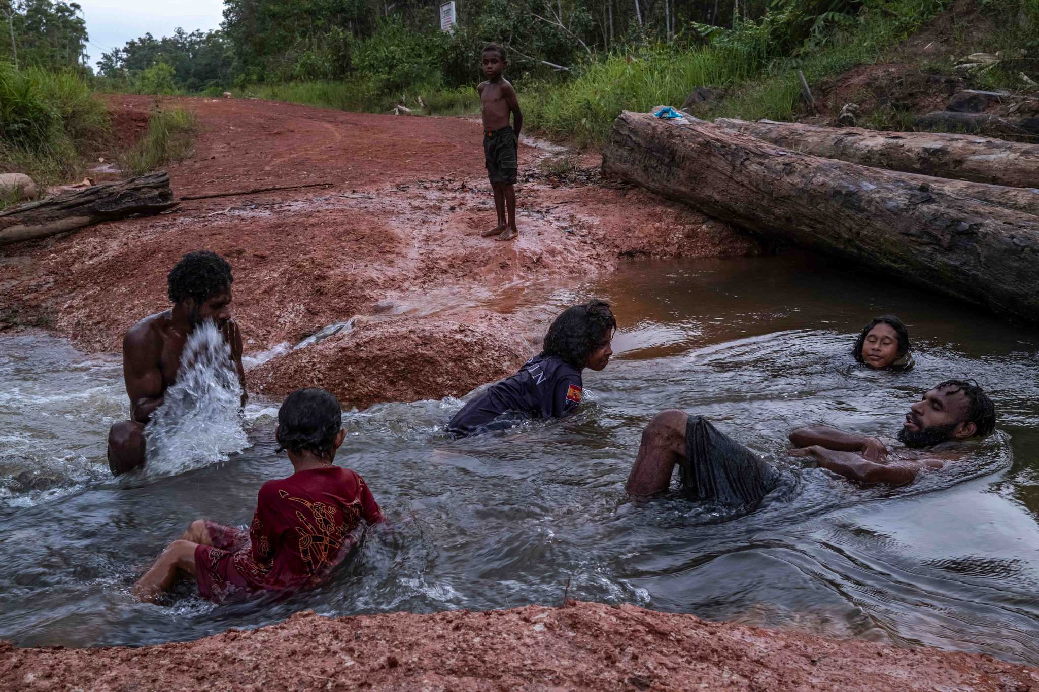 People swimming in a river next to a muddy road