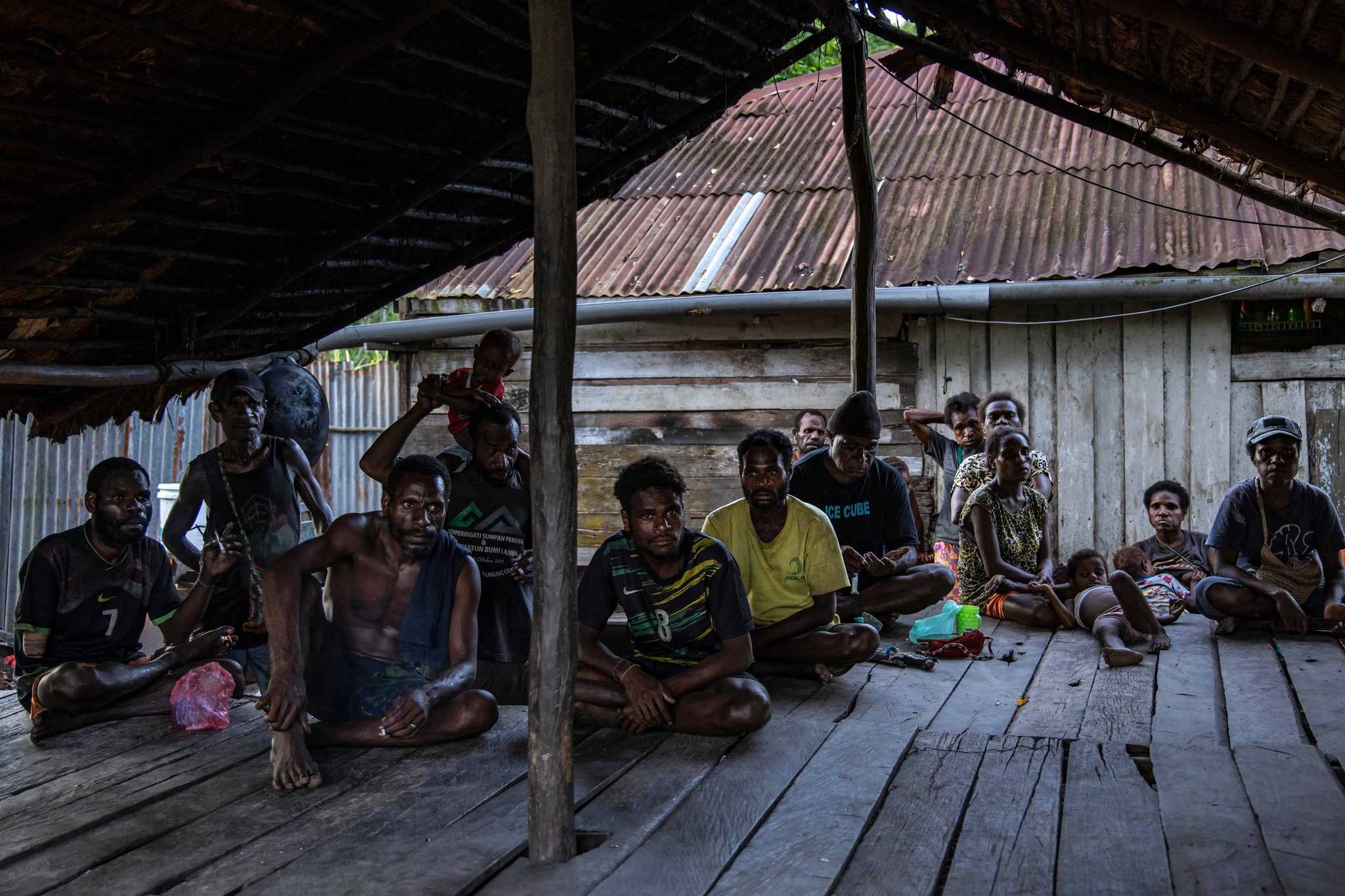 A group of Papuan people sit inside a wooden structure.